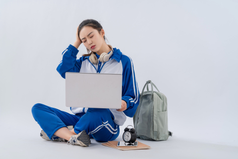 坐地上手拿笔记本认真思考的学生实拍图